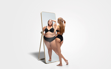 Image showing Young slim woman looking at fat girl in mirror\'s reflection on white background