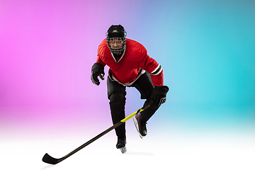 Image showing Male hockey player with the stick on ice court and neon colored gradient background. Sportsman wearing equipment, helmet practicing.