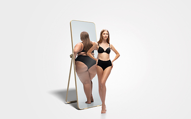 Image showing Young slim woman looking at fat girl in mirror\'s reflection on white background