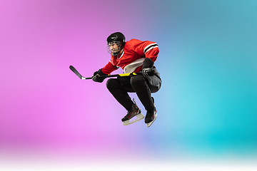 Image showing Male hockey player with the stick on ice court and neon colored gradient background. Sportsman wearing equipment, helmet practicing.