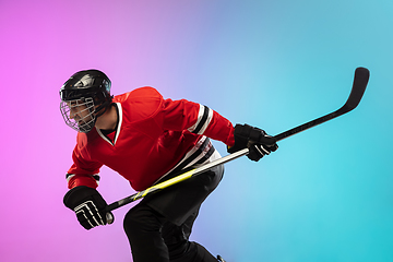 Image showing Male hockey player with the stick on ice court and neon colored gradient background. Sportsman wearing equipment, helmet practicing.