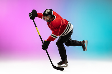 Image showing Male hockey player with the stick on ice court and neon colored gradient background. Sportsman wearing equipment, helmet practicing.
