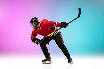 Image showing Male hockey player with the stick on ice court and neon colored gradient background. Sportsman wearing equipment, helmet practicing.