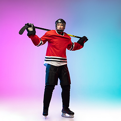 Image showing Male hockey player with the stick on ice court and neon colored gradient background. Sportsman wearing equipment, helmet practicing.