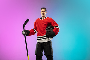 Image showing Male hockey player with the stick on ice court and neon colored gradient background. Sportsman wearing equipment, helmet practicing.