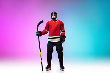 Image showing Male hockey player with the stick on ice court and neon colored gradient background. Sportsman wearing equipment, helmet practicing.