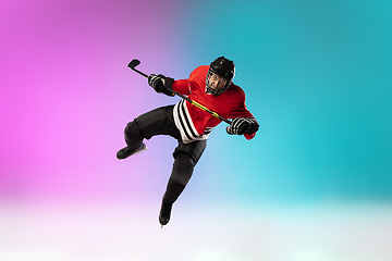 Image showing Male hockey player with the stick on ice court and neon colored gradient background. Sportsman wearing equipment, helmet practicing.