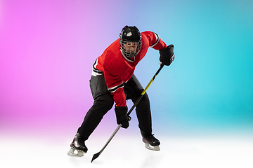 Image showing Male hockey player with the stick on ice court and neon colored gradient background. Sportsman wearing equipment, helmet practicing.