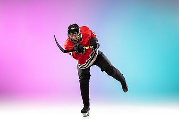 Image showing Male hockey player with the stick on ice court and neon colored gradient background. Sportsman wearing equipment, helmet practicing.