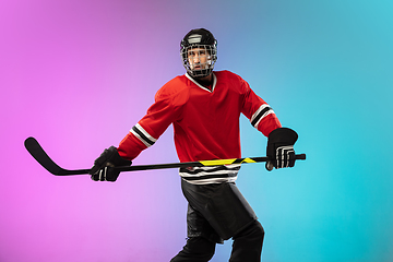 Image showing Male hockey player with the stick on ice court and neon colored gradient background. Sportsman wearing equipment, helmet practicing.