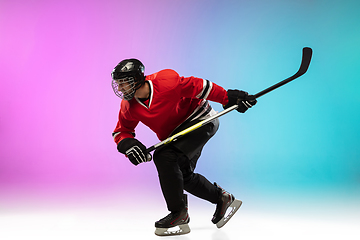 Image showing Male hockey player with the stick on ice court and neon colored gradient background. Sportsman wearing equipment, helmet practicing.