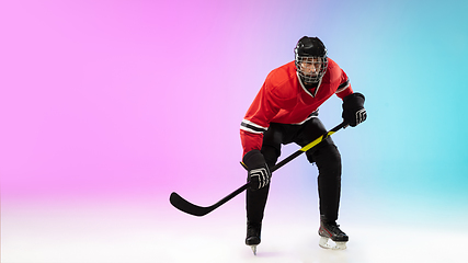 Image showing Male hockey player with the stick on ice court and neon colored gradient background. Sportsman wearing equipment, helmet practicing.