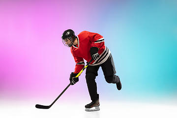 Image showing Male hockey player with the stick on ice court and neon colored gradient background. Sportsman wearing equipment, helmet practicing.