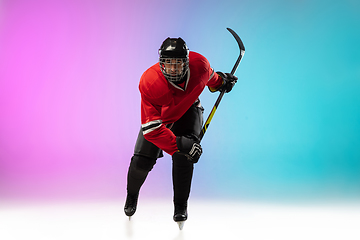 Image showing Male hockey player with the stick on ice court and neon colored gradient background. Sportsman wearing equipment, helmet practicing.