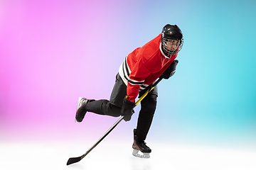 Image showing Male hockey player with the stick on ice court and neon colored gradient background. Sportsman wearing equipment, helmet practicing.