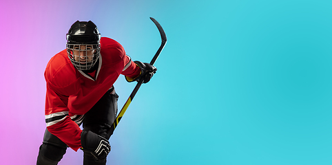 Image showing Male hockey player with the stick on ice court and neon colored gradient background. Sportsman wearing equipment, helmet practicing.