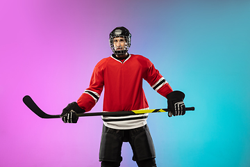 Image showing Male hockey player with the stick on ice court and neon colored gradient background. Sportsman wearing equipment, helmet practicing.