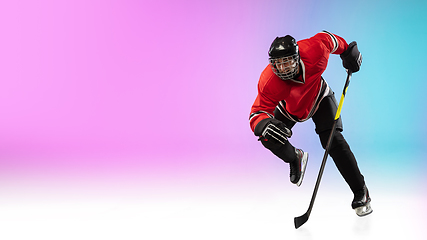 Image showing Male hockey player with the stick on ice court and neon colored gradient background. Sportsman wearing equipment, helmet practicing.