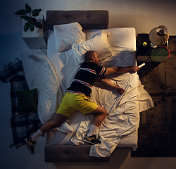 Image showing Top view of young professional tennis player sleeping at his bedroom in sportwear with racket