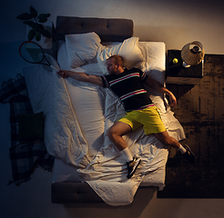 Image showing Top view of young professional tennis player sleeping at his bedroom in sportwear with racket