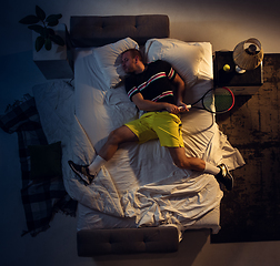 Image showing Top view of young professional tennis player sleeping at his bedroom in sportwear with racket