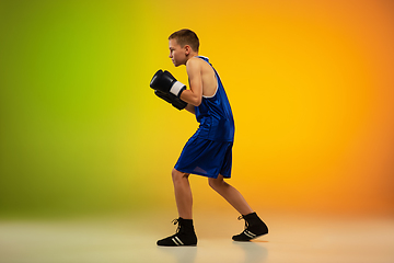 Image showing Teenage boxer against gradient neon studio background in motion of kicking, boxing