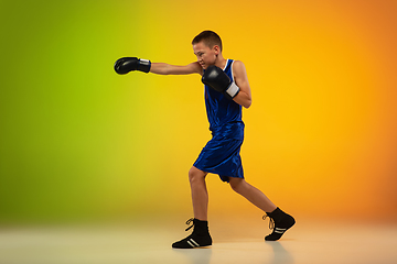 Image showing Teenage boxer against gradient neon studio background in motion of kicking, boxing