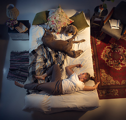 Image showing Portrait of a woman, female breeder sleeping in the bed with her dog at home