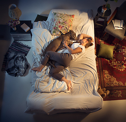 Image showing Portrait of a woman, female breeder sleeping in the bed with her dog at home