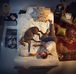 Image showing Portrait of a woman, female breeder sleeping in the bed with her dog at home