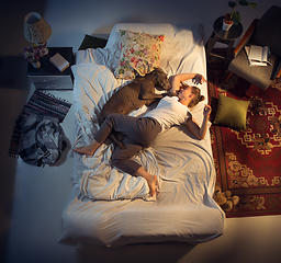 Image showing Portrait of a woman, female breeder sleeping in the bed with her dog at home