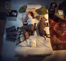 Image showing Portrait of a woman, female breeder sleeping in the bed with her dog at home