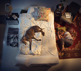 Image showing Portrait of a woman, female breeder sleeping in the bed with her dog at home