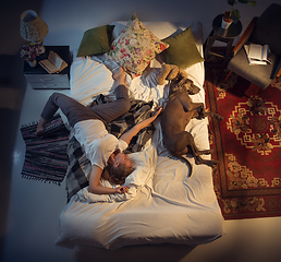 Image showing Portrait of a woman, female breeder sleeping in the bed with her dog at home