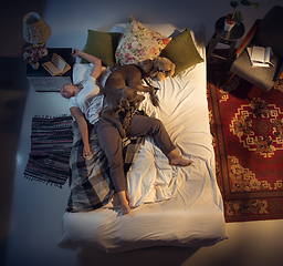 Image showing Portrait of a woman, female breeder sleeping in the bed with her dog at home