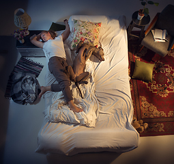 Image showing Portrait of a woman, female breeder sleeping in the bed with her dog at home