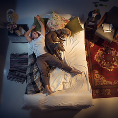 Image showing Portrait of a woman, female breeder sleeping in the bed with her dog at home