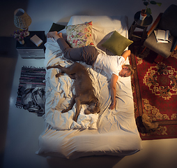 Image showing Portrait of a woman, female breeder sleeping in the bed with her dog at home