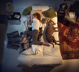 Image showing Portrait of a woman, female breeder sleeping in the bed with her dog at home