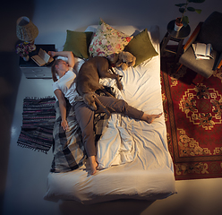 Image showing Portrait of a woman, female breeder sleeping in the bed with her dog at home