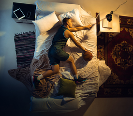 Image showing Top view of young professional basketball player sleeping at his bedroom in sportwear with ball