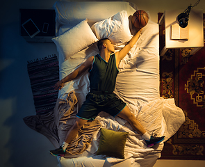 Image showing Top view of young professional basketball player sleeping at his bedroom in sportwear with ball