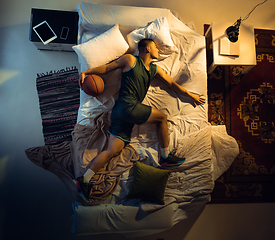 Image showing Top view of young professional basketball player sleeping at his bedroom in sportwear with ball