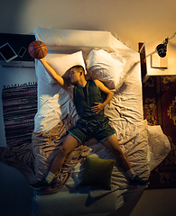 Image showing Top view of young professional basketball player sleeping at his bedroom in sportwear with ball