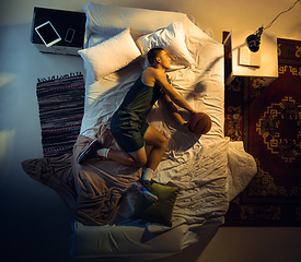 Image showing Top view of young professional basketball player sleeping at his bedroom in sportwear with ball