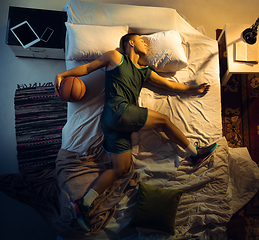 Image showing Top view of young professional basketball player sleeping at his bedroom in sportwear with ball