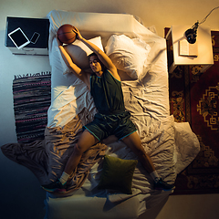 Image showing Top view of young professional basketball player sleeping at his bedroom in sportwear with ball