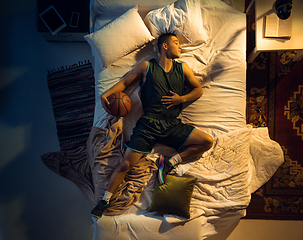 Image showing Top view of young professional basketball player sleeping at his bedroom in sportwear with ball