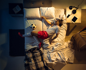 Image showing Top view of young professional football, soccer player sleeping at his bedroom in sportwear with ball