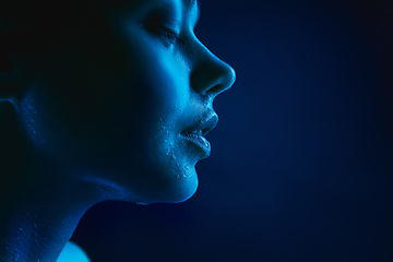 Image showing Portrait of female fashion model in neon light on dark studio background.